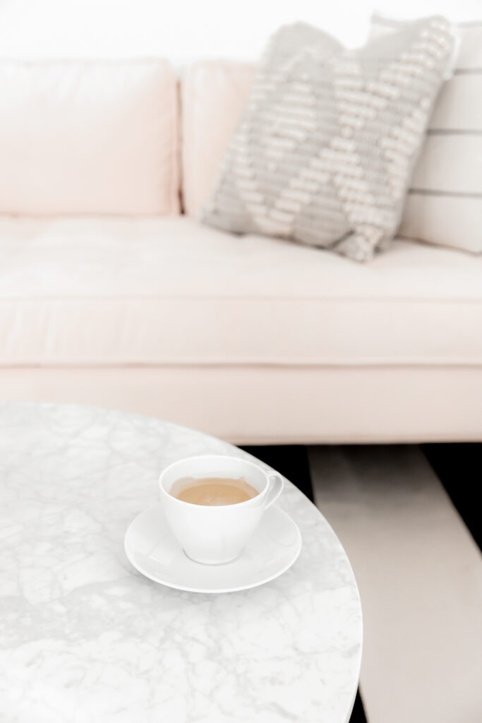pink couch with throw pillows and a marble topped coffee table with a latte
