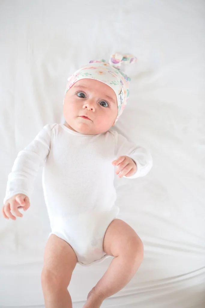 baby girl in white onesie and floral hat