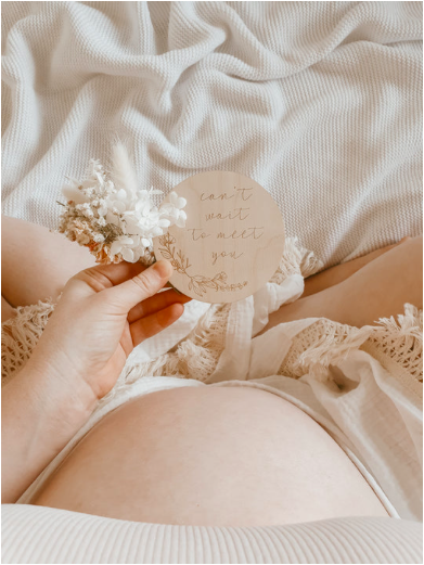 pregnant woman showing bump and holding milestone card