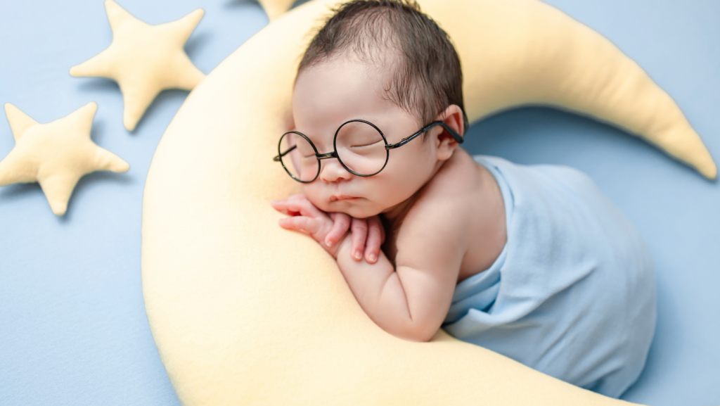 newborn baby in glasses sleeping on a stuffed moon 